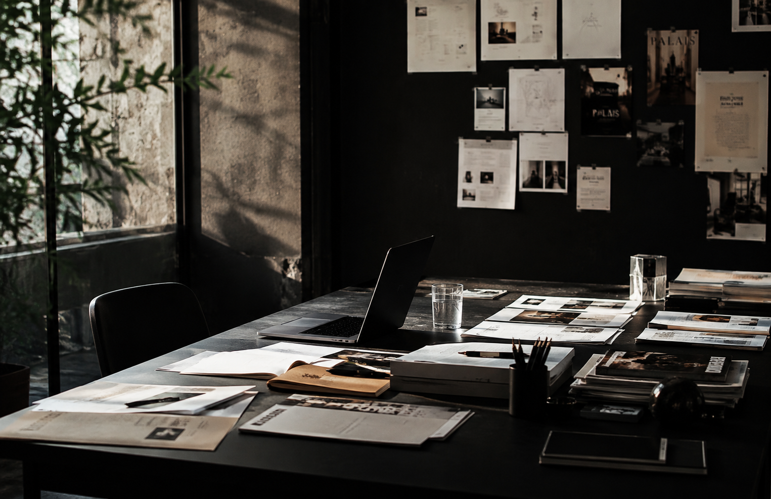 A notebook labeled Campaign Concepts open on a desk, with handwritten notes, a pen, a glass of water, and contact-sheet prints